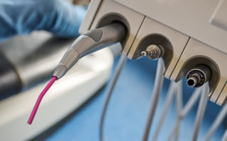 Zahnarztinstrumente mit Schläuchen und einem Handstück, das aus einer Halterung ragt, im Vordergrund.